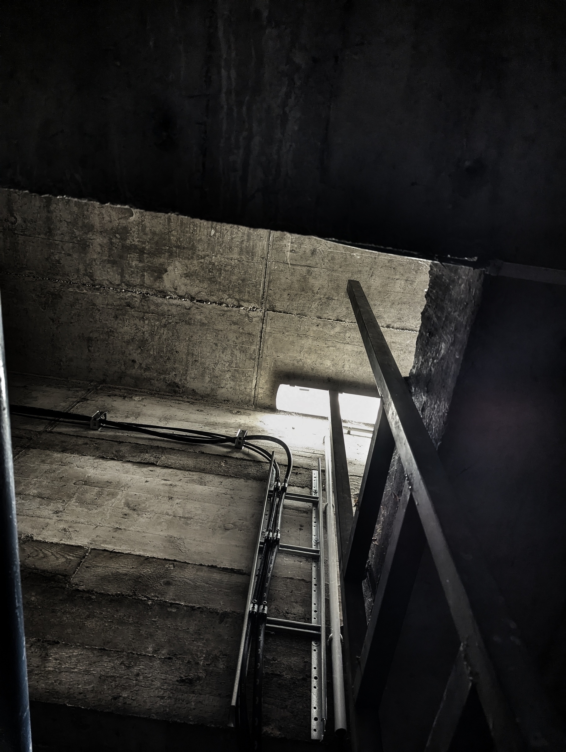 A ladder teaching upwards. Again, dark, grey, concrete, dead