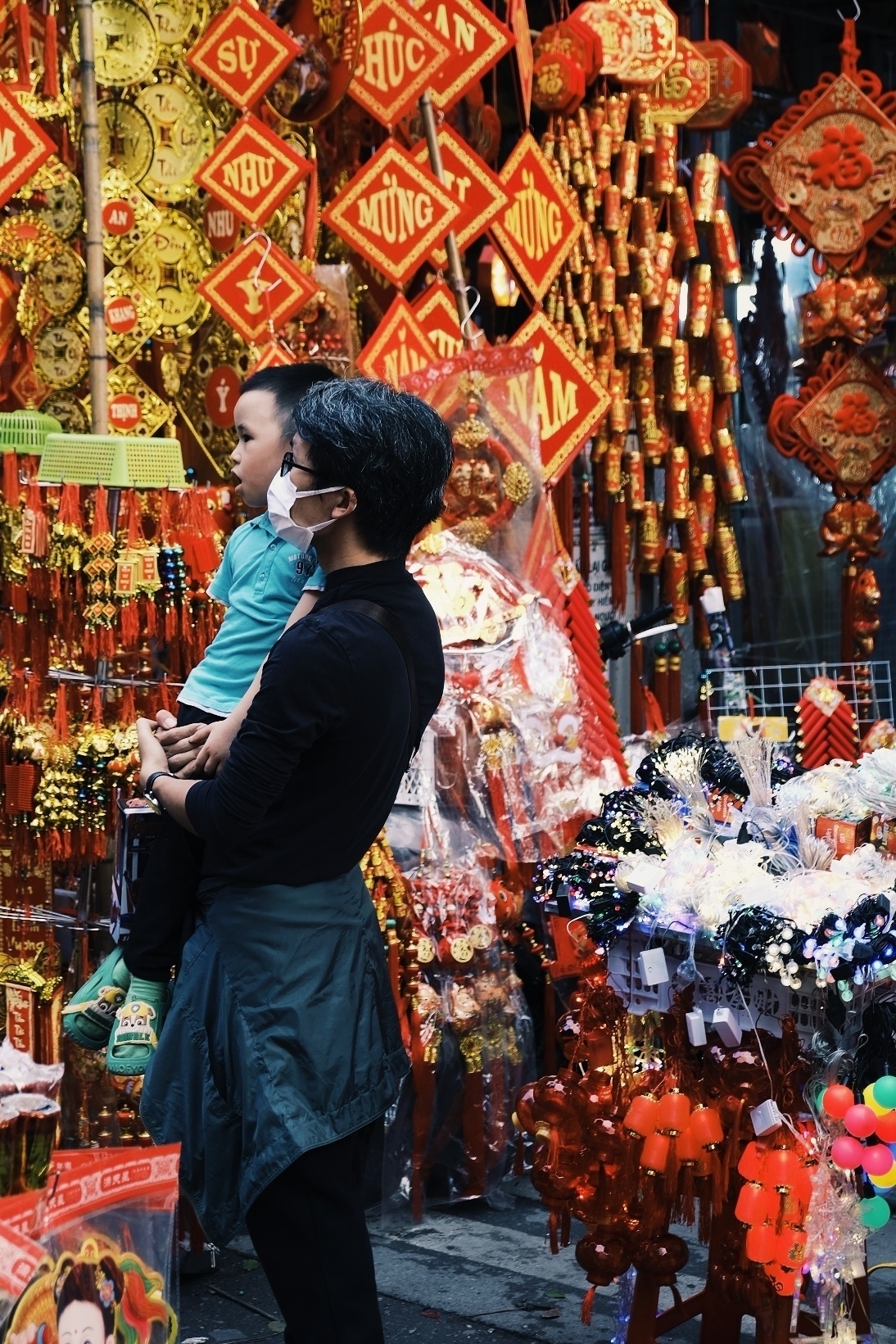 A mother wearing a mask and her child in front of colourful Tet decoration. It's the year of the dragon, expect it to be a fire
