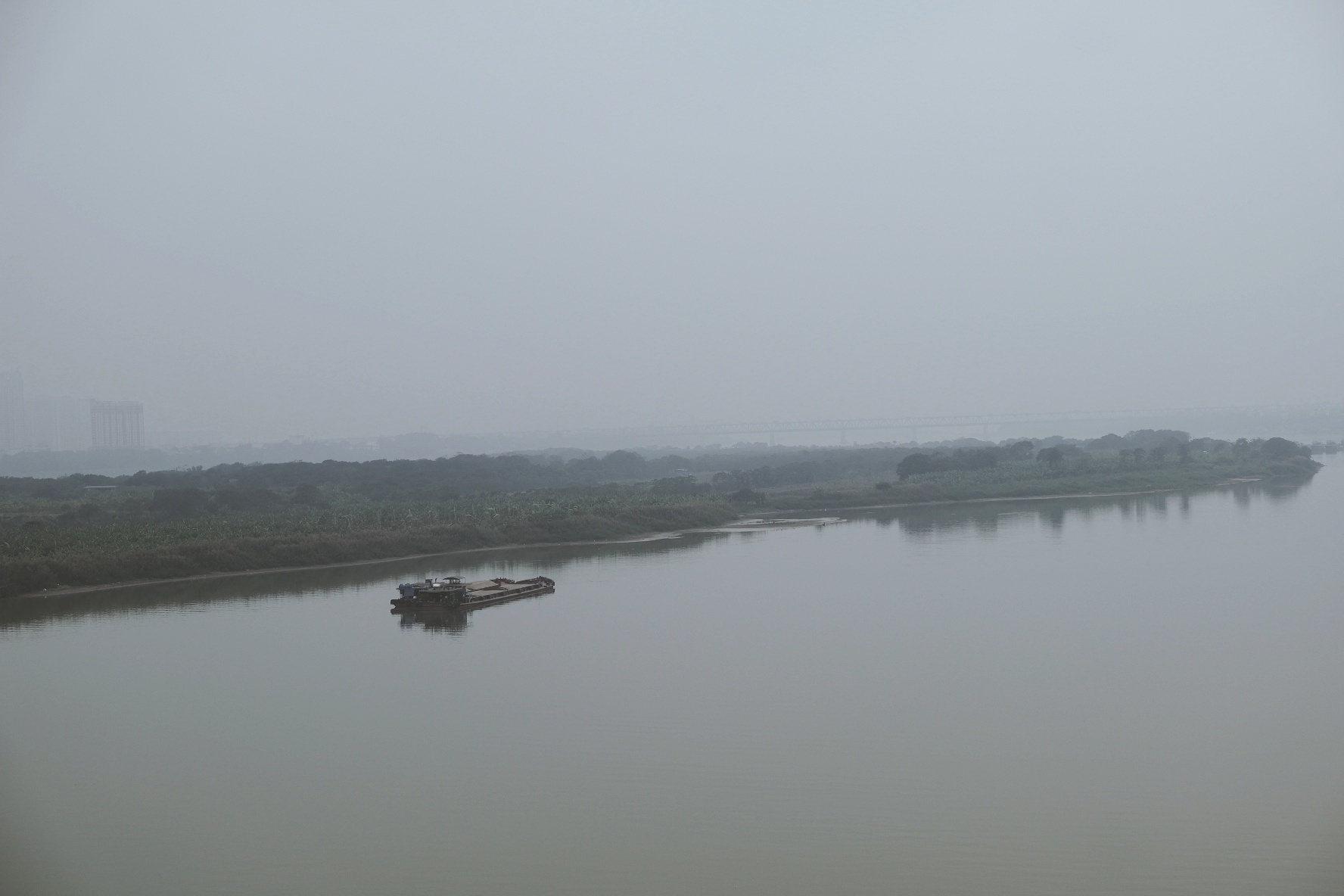 The view of the red river (and delta) from the highway bridge. Again, foggy. Sky and water merge. There's a boat floating, carrying sand of sorts 